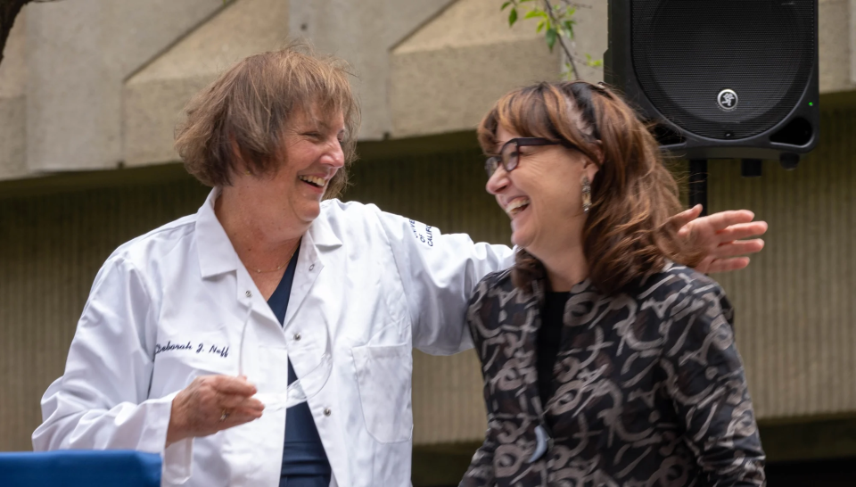 Neff, left in a white lab coat and holding safety glasses, with Kimberley McAllister, director of the Center for Neuroscience.