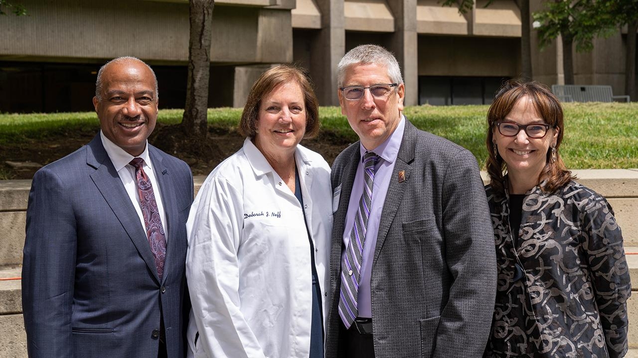 Chancellor Gary May, Deb Neff, Dean Mark Winey and Kimberly McAllister pose for a photo outside in front of a university campus building with a green lawn.